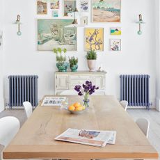 wooden dining table with white chairs in bright white dining room with gallery wall and radiators