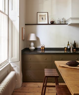 accent colors for a white kitchen, white kitchen with black countertop, dark sage green units, large wood table, wooden floorboards, shutters at window