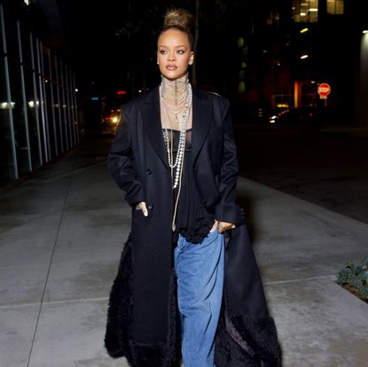 Rihanna in lingerie, blue jeans, pearl necklaces, and a black maxi coat