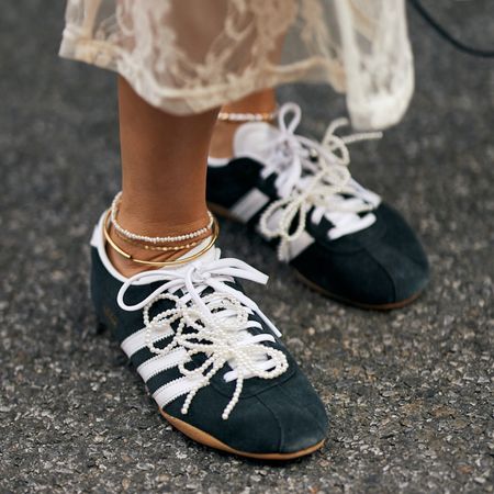 woman wearing black and white adidas sneakers with pearl laces and anklets 