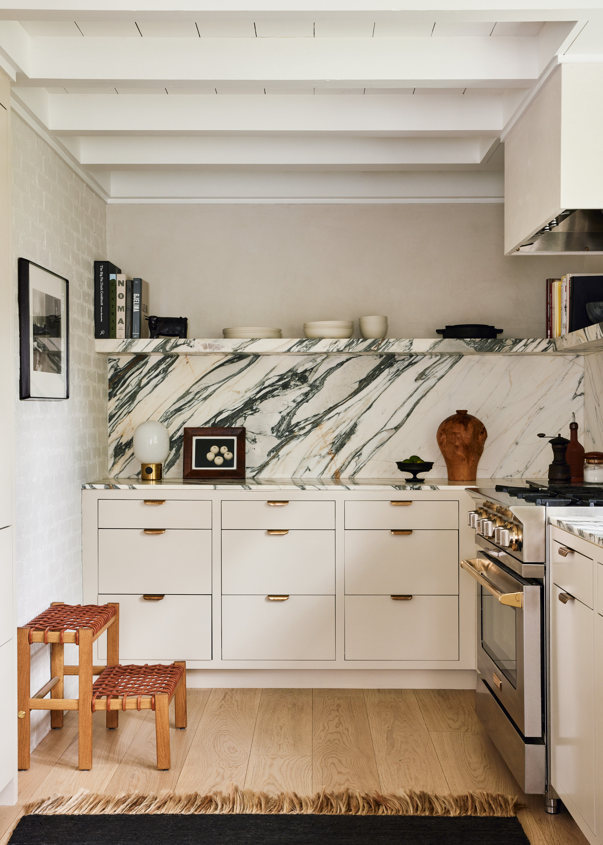 Kitchen with white cabinetry, veined marble splashback and shelving, wood and woven leather step stool