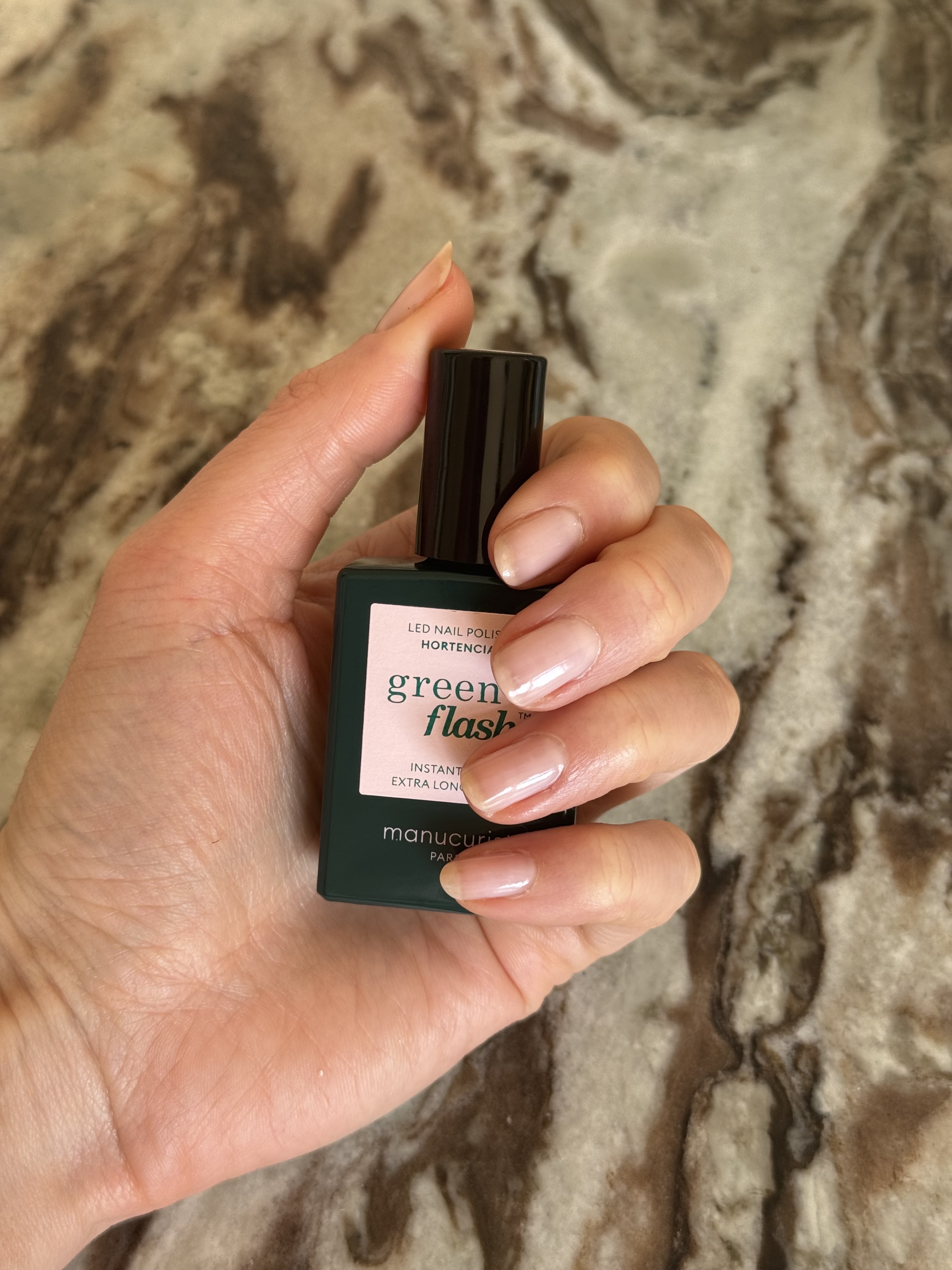 Eleanor holding a bottle of Manucurist Hortencia Green Flash nail polish, with her fingernails painted in the same glossy sheer pink nail colour