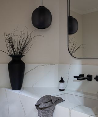 Quartz basin and backsplash, pale pink walls, black accents of vase, mirror, pendant light,