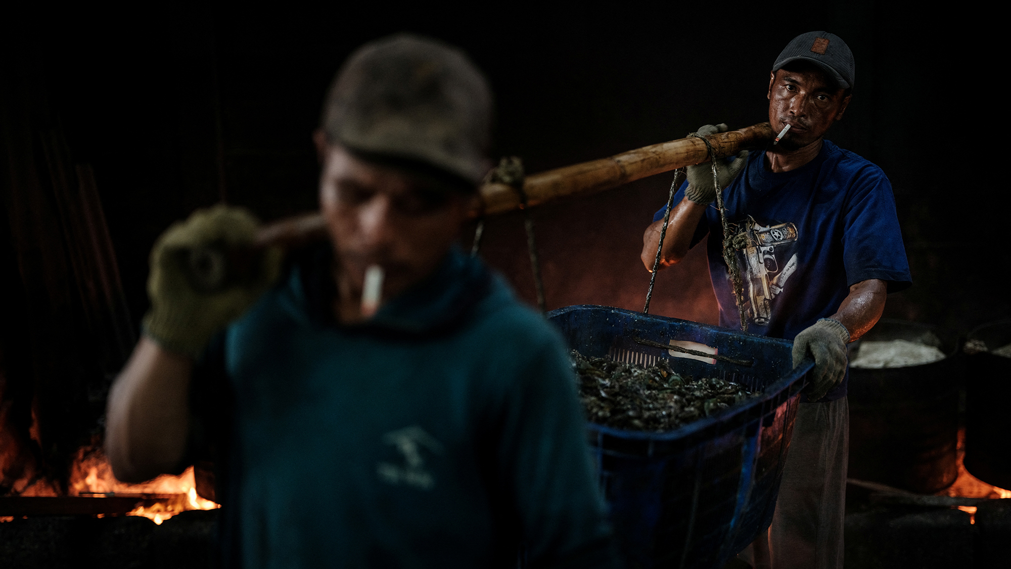 Workers carry a basket of freshly boiled green mussels at a processing site in Cilincing, North Jakarta