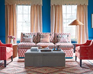 A blue living room with red armchairs, red and white sofa and wicker lamp