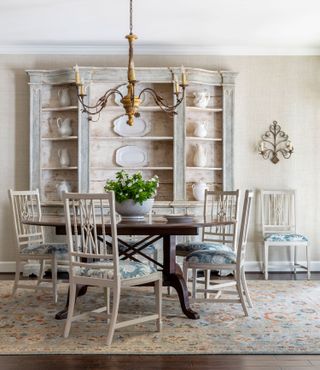 dining room with pale blue walls and grey painted dining chairs and glazed cabinet with dark wood round table and oriental style rug on dark wood floor and chandelier