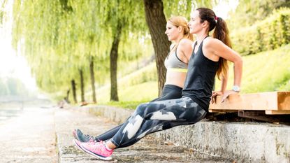 Two women doing triceps dips outdoors.