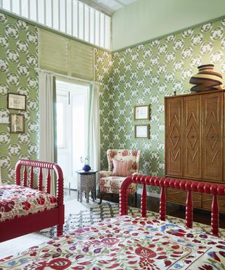 A bedroom with green and white patterned wallpaper and red-framed twin beds