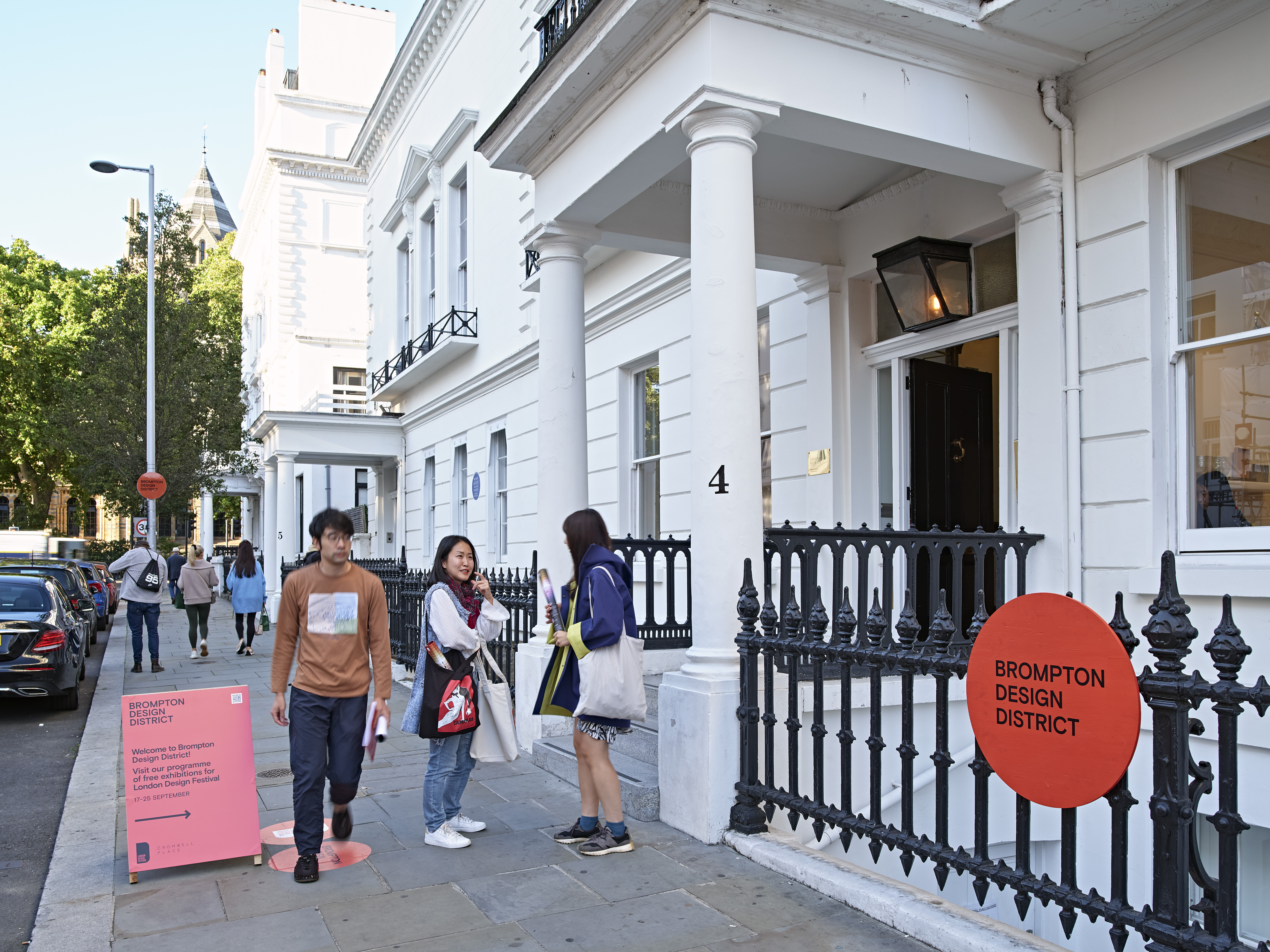 People walking and standing on a west London street next to the entrance of a white building