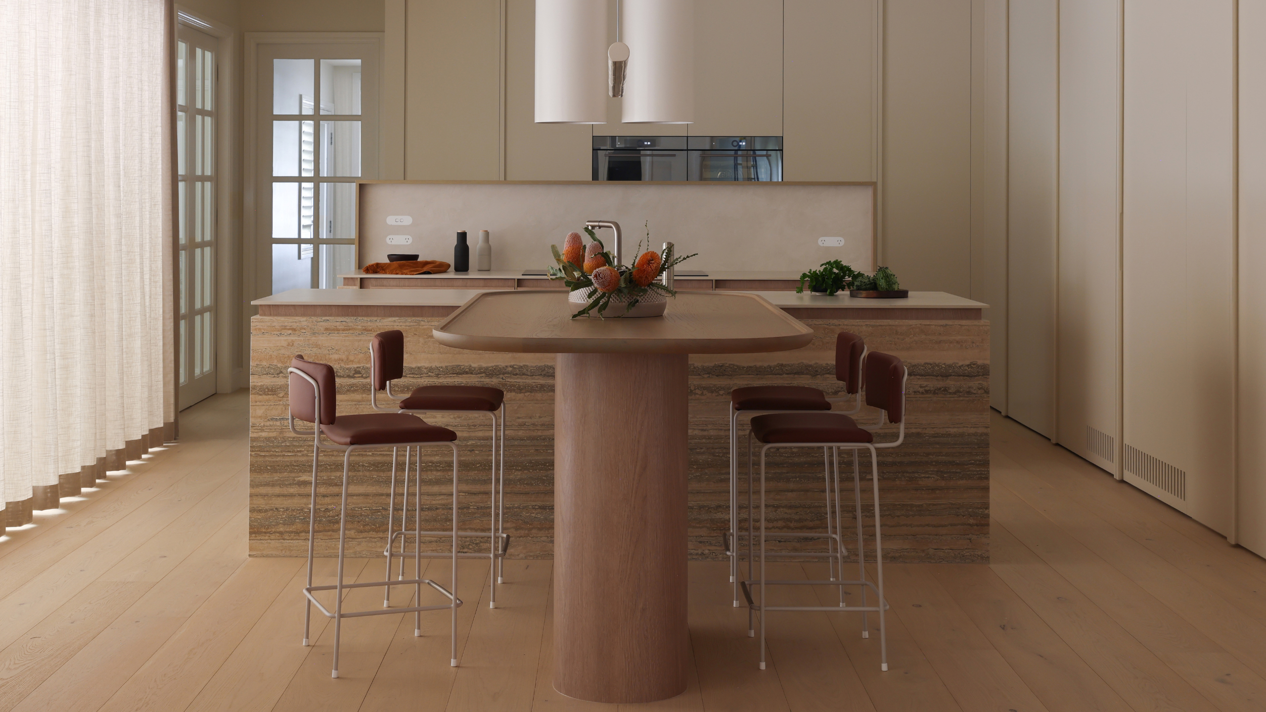 A minimalist open layout dining room and kitchen with maroon stools with a white frame, a marble island, a white exhaust above, and a floral centrepiece