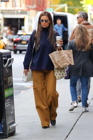 Katie Holmes in New York City wearing a navy blue turtleneck, plaid pants, and black boots while getting a coffee and picking up Eataly.