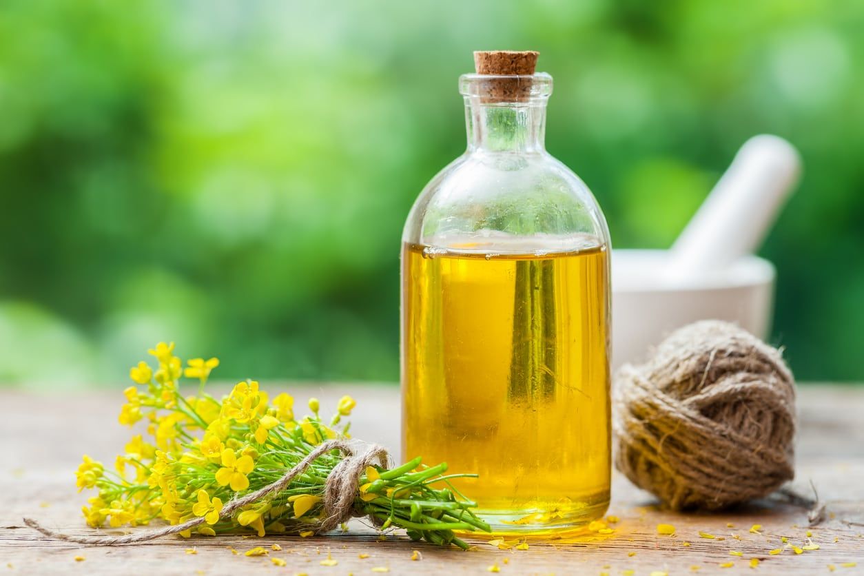 Glass Jar Of Canola Oil Next To Yellow Flowers