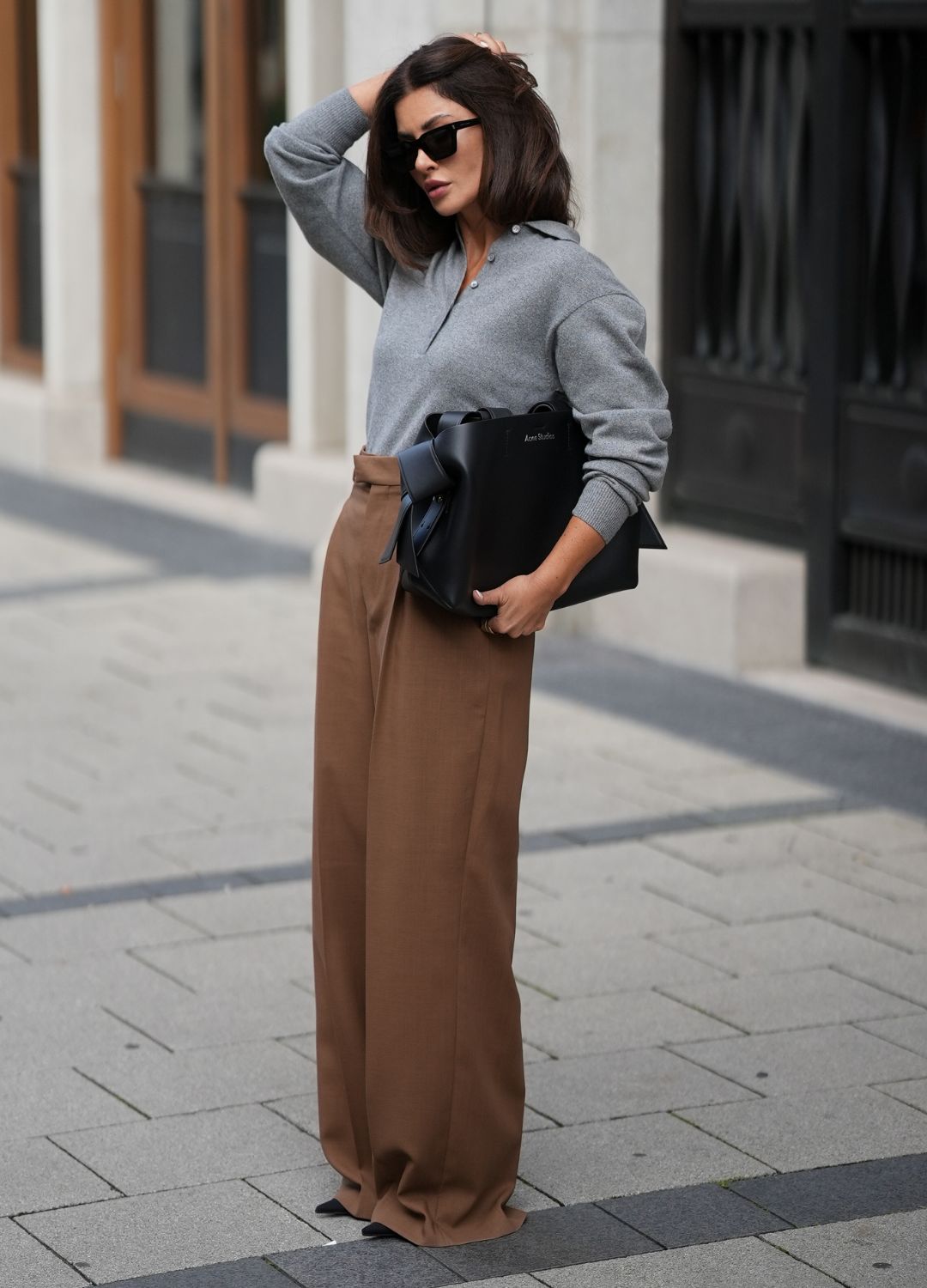 F&amp;uuml;sun Lindner is seen wearing a grey long-sleeve knit polo with a half-button placket, worn tucked into the trousers from Stella McCartney; high-waisted wide-leg trousers in a warm camel-brown shade, draping fluidly to the shoes from Ami Paris; black pointed-toe high heels from Balenciaga; a large structured black leather handbag, with silver minimal branding and details from Acne; black rectangular sunglasses with a sharp silhouette from Saint Laurent; her brown hair is worn in a sleek, straight bob with a middle part on September 3, 2025 in Munich, Germany.