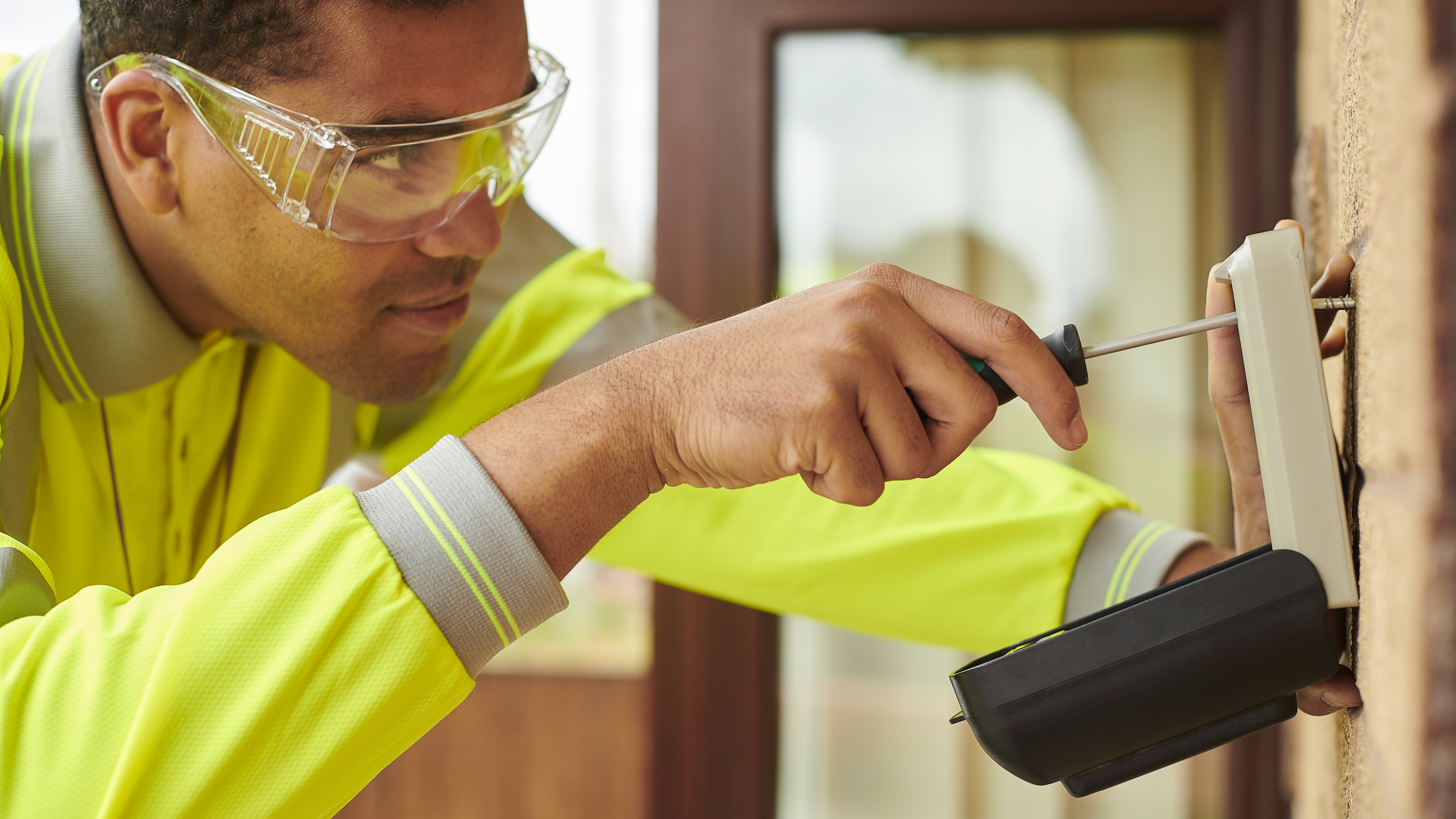 Head and shoulders photo of man in hi vis jacket screwing key safe into brick wall