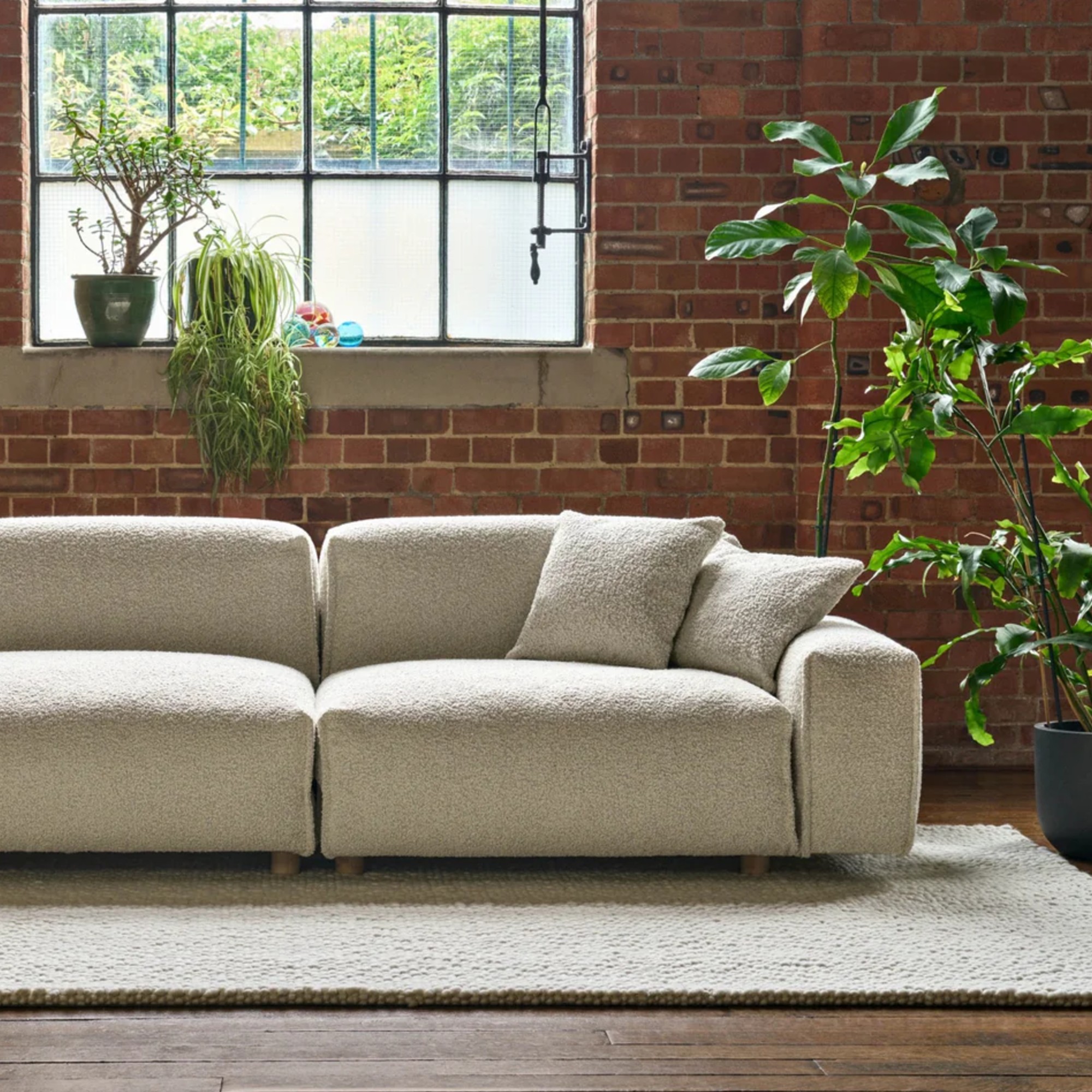 The Cozmo Float sofa in cream boucle in a living room with exposed brick walls and large plants