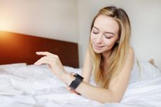 Woman looking at smartwatch laying on white bed