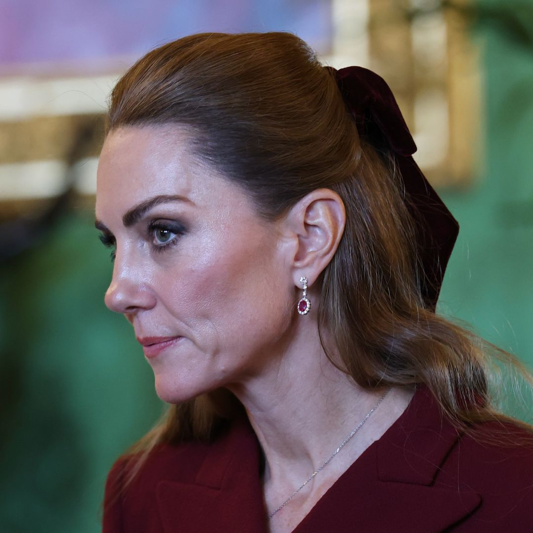 Princess Kate in a burgundy coat and hair bow looking serious 