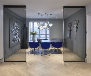 open plan dining room with blue chairs, smoked glass panels and parquet floors