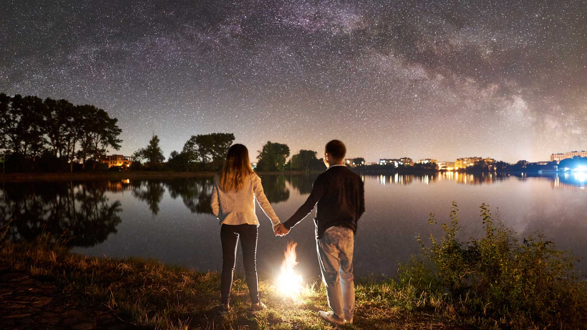The men are holding hands in the lake under the night sky