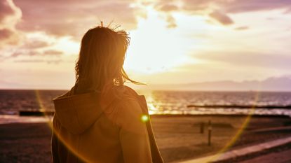 A woman looks toward the sunrise over the water at the beach.