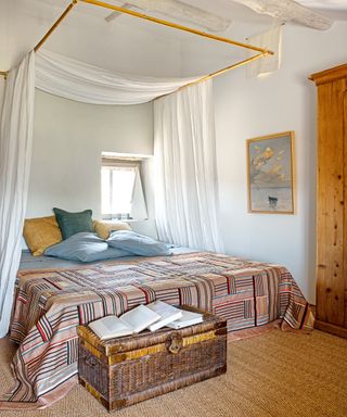 guest bedroom with patterned throw, blue and ochre cushions, woven floorcovering and woven trunk