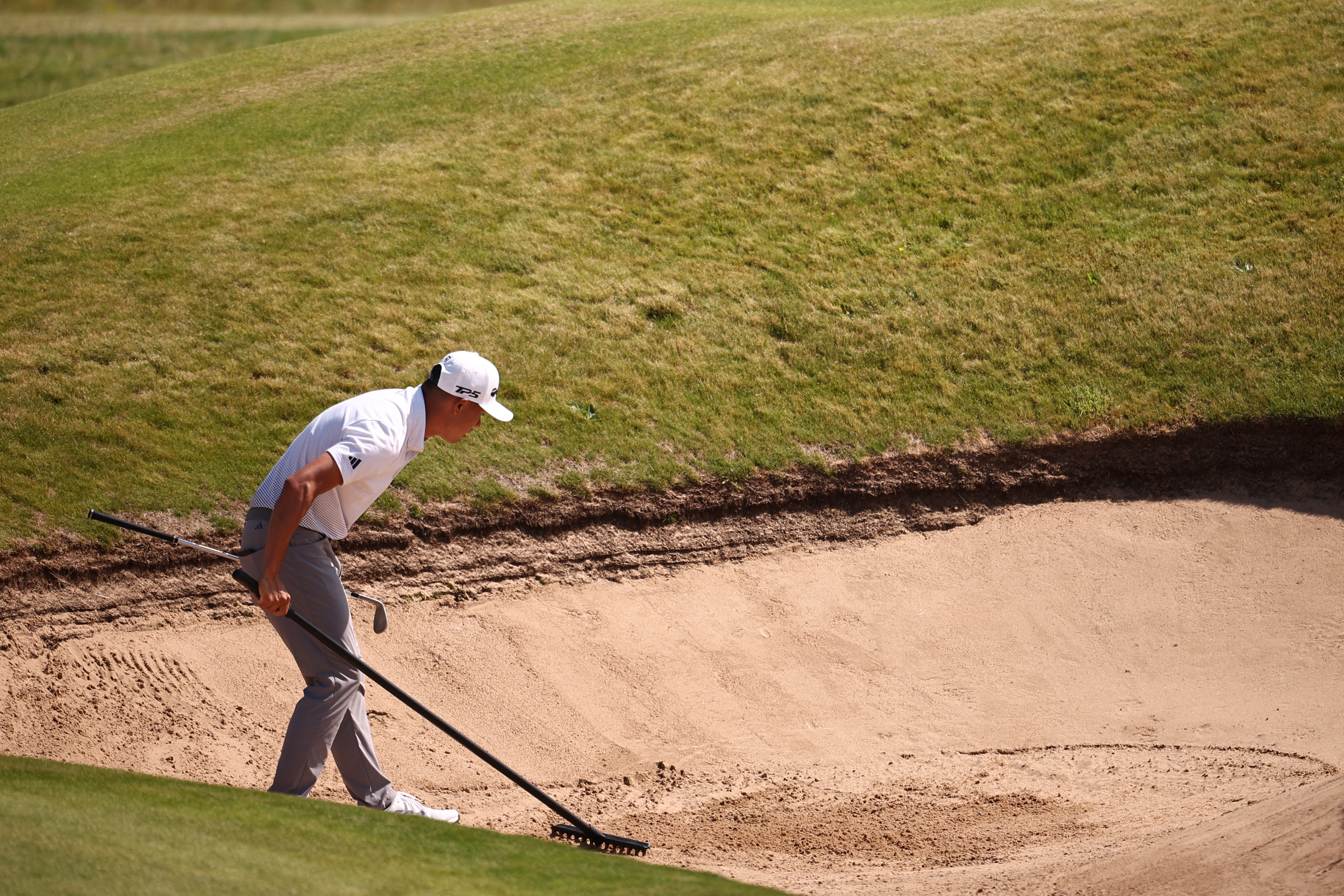 Collin Morikawa rakes a bunker