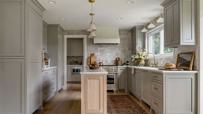A kitchen with gray cabinets, a wooden island, zellige wall tiles, and brass hardware