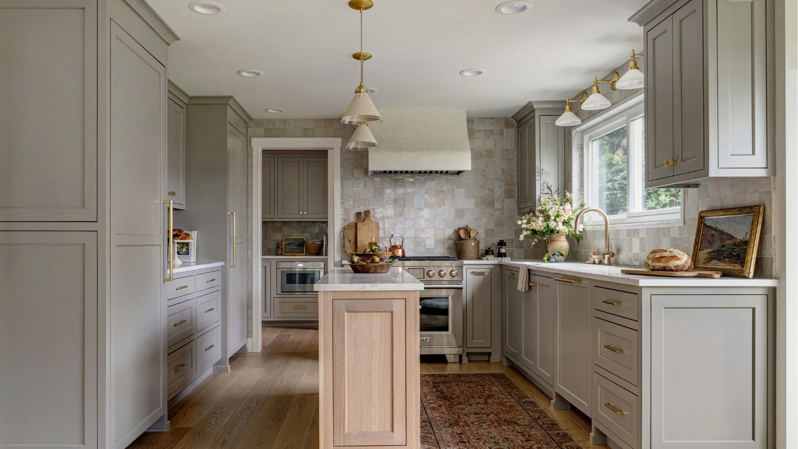 A kitchen with gray cabinets, a wooden island, zellige wall tiles, and brass hardware