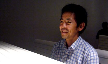 A photo of Yoshiharu Tsukamoto wearing a checkered blue and white button down collar shirt. 