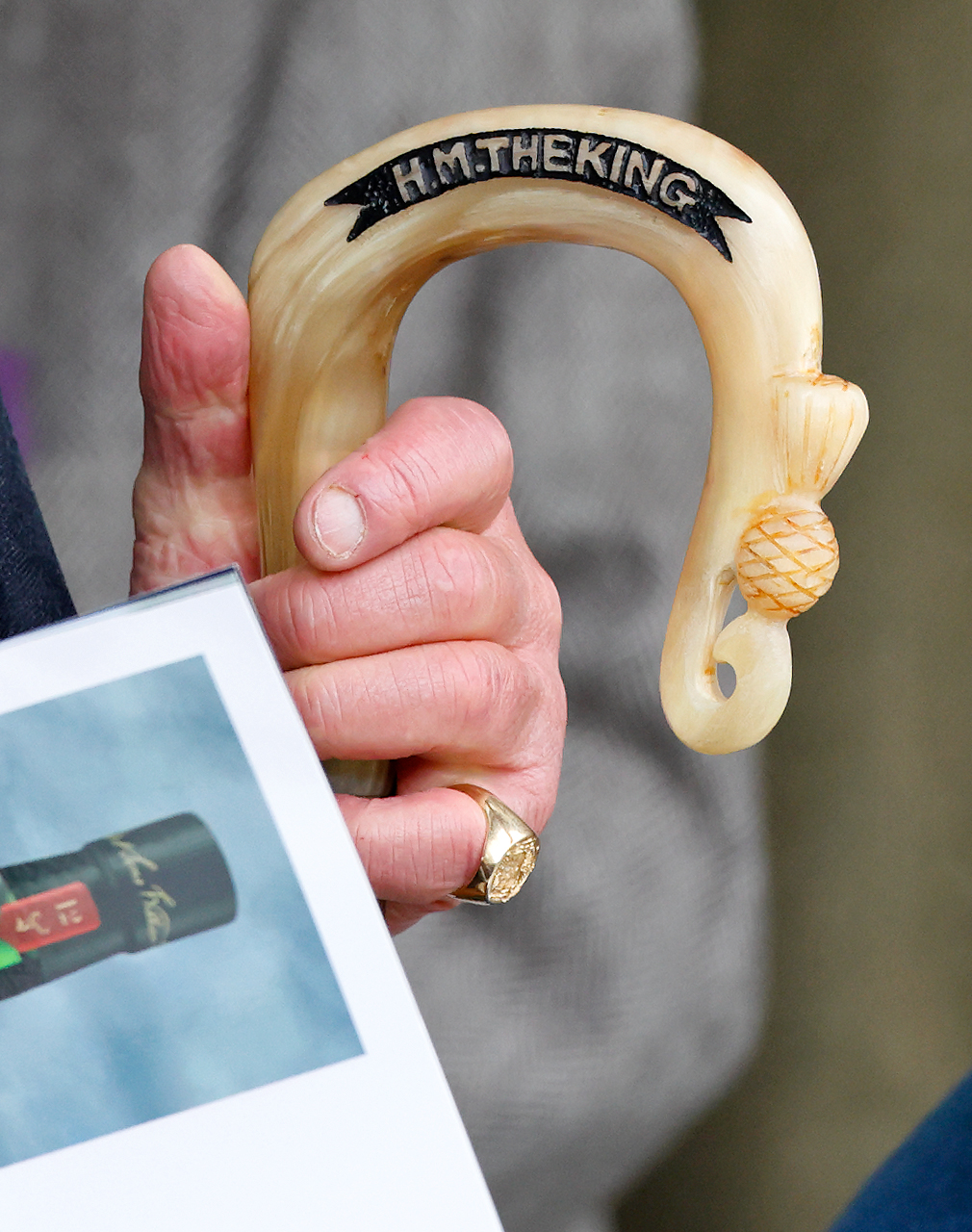 King Charles's hand holding a walking stick that reads HM The King