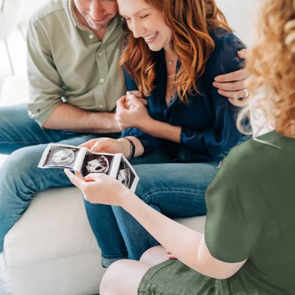 Expecting parents meet with a surrogate, who is holding sonogram photos.