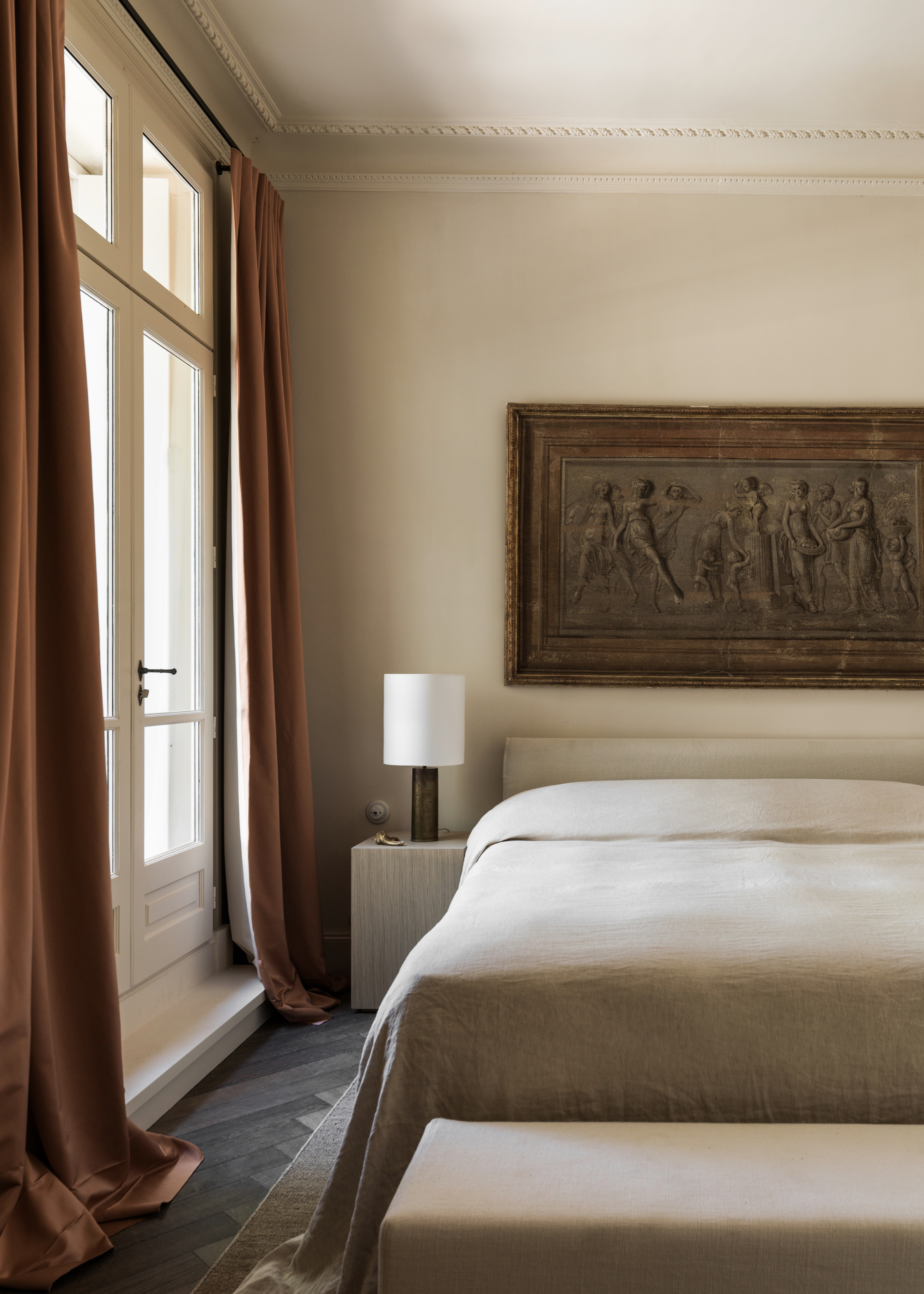 A cream bedroom with flowing curtains, a framed painting, a muted bedscape