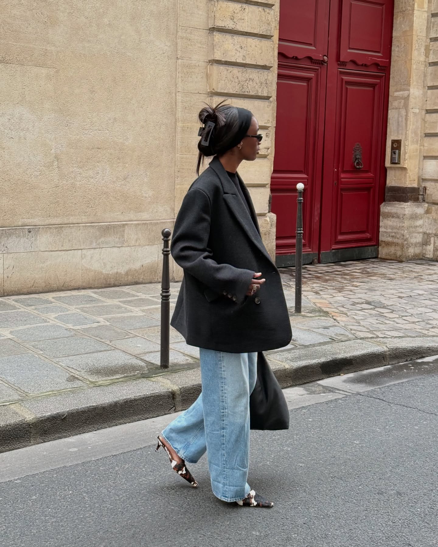 Influencer @_livmadeline walks outside wearing wide-leg jeans, a black blazer and pointed-toe heels.
