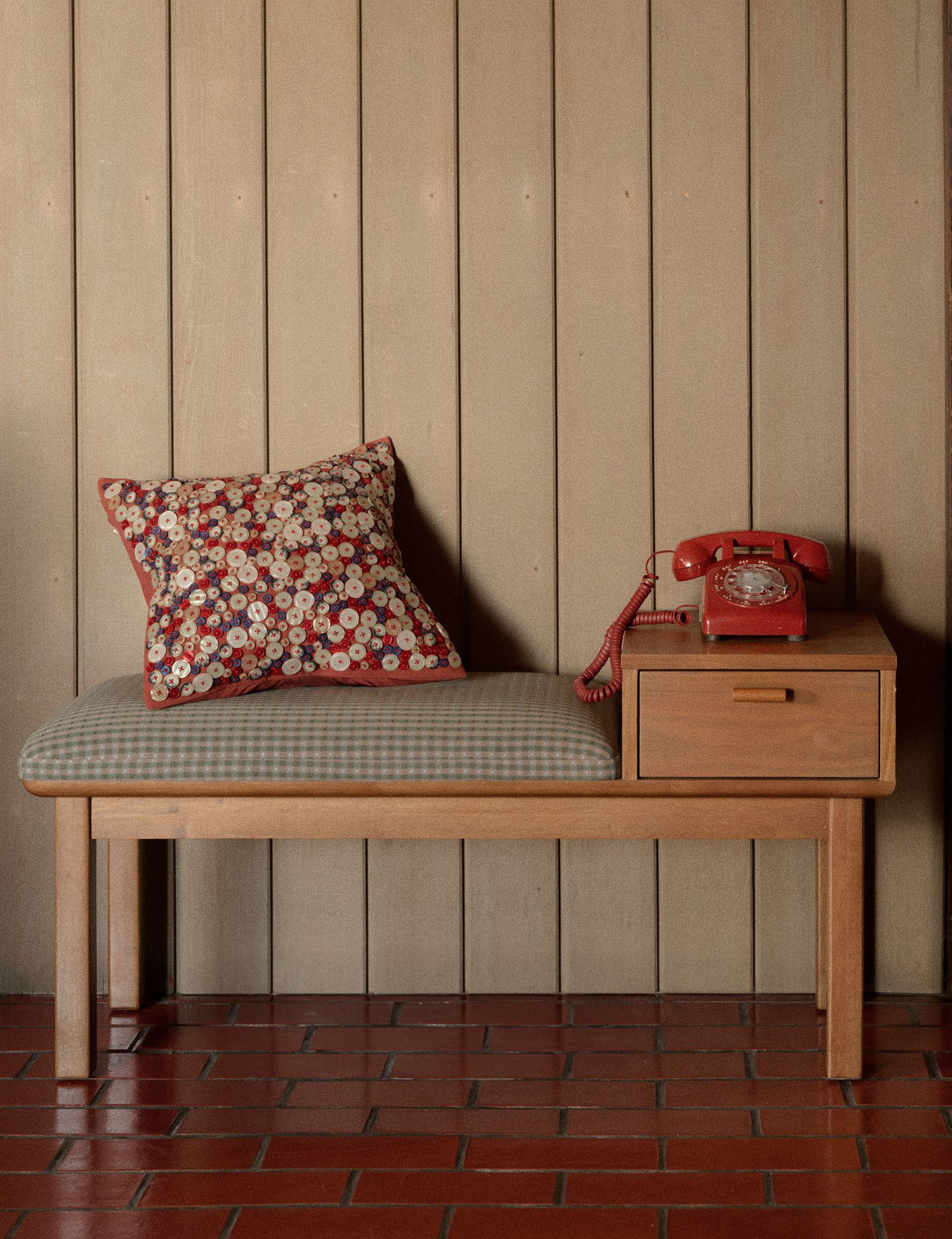 Mid-century-style telephone bench topped with a button-embellished pillow and red landline phone.