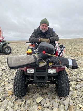 Rod Pyle sits astride an ATV in a rocky Arctic landscape.