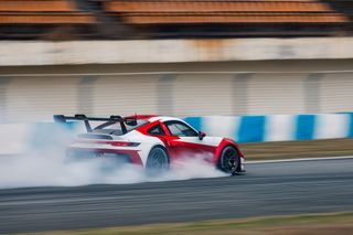 Red and white race car in motion creating tire smoke on a track