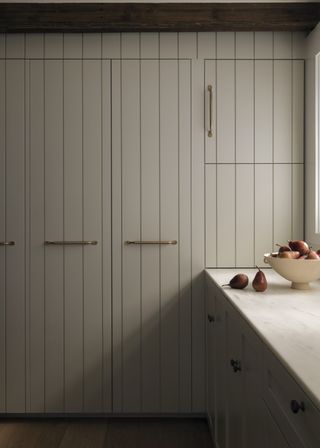 A kitchen with cupboards and lower cabinets. On the countertop is a bowl with fruits inside of it