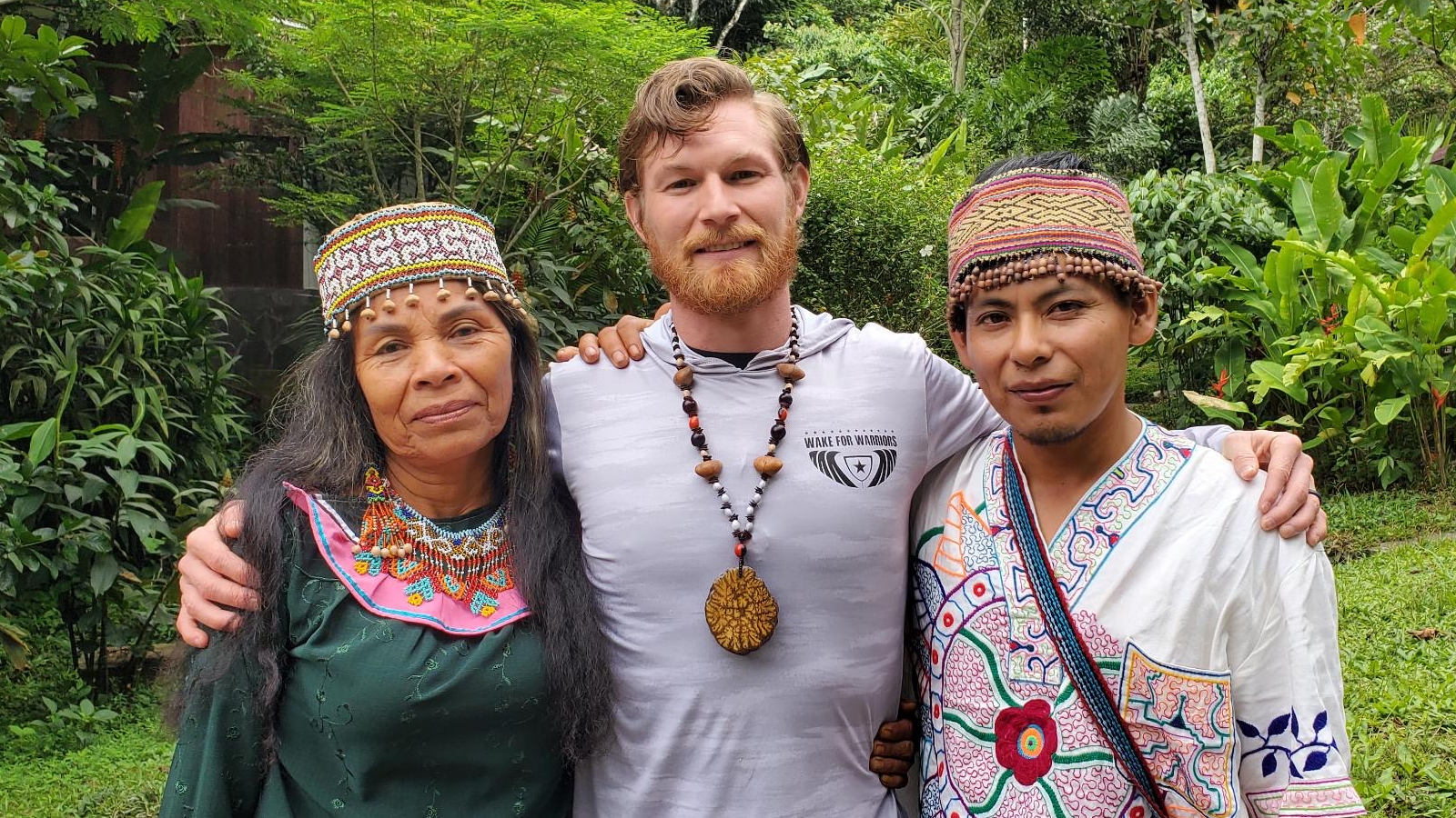 Three people stand together in a green area with lots of plants.