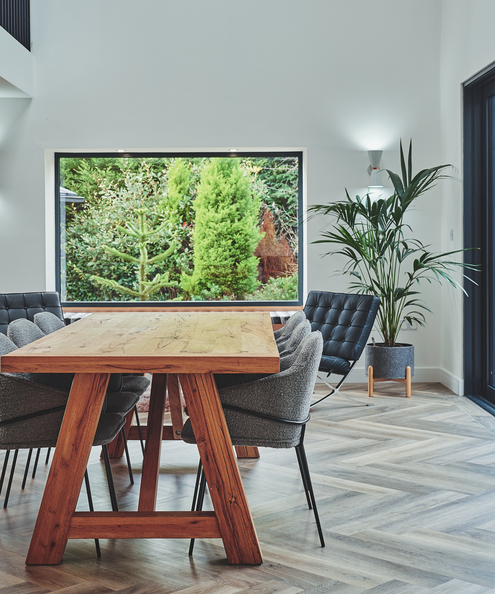 herringbone laid wooden flooring in dining room with wooden table, upholstered chairs and large picture window