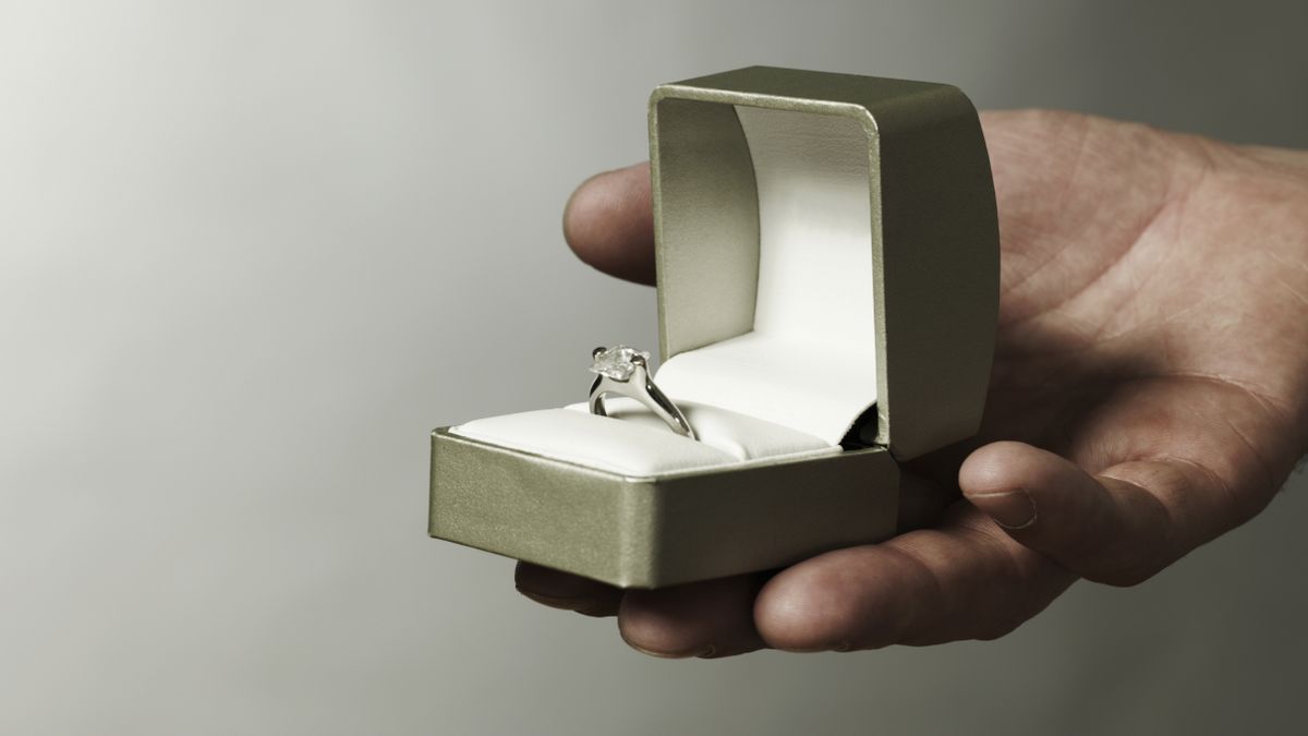 A hand holds out an engagement ring