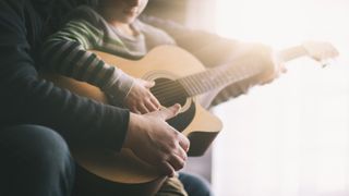Best guitars for kids: man teaches son how to play acoustic guitar