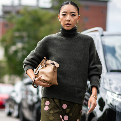 A guest attends milan spring summer 2025 fashion week wearing grey turtleneck sweater, green and pink sequin skirt, and carrying beige handbag