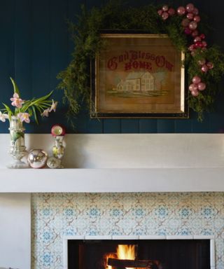 Mantelpiece with white fireplace, dark blue upper wall with artwork and festive foliage decor