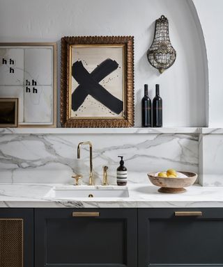A stylish kitchen sink area with a marble backsplash and worktops with open shelving above
