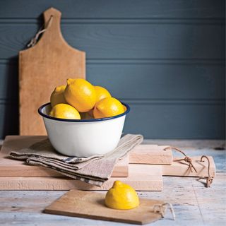 Bowl of lemons with one cut lemon on wooden chopping board