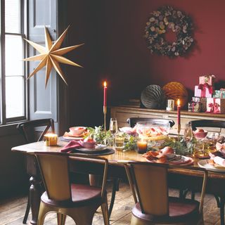 A burgundy-painted dining room with a set table for dinner with lit candles and pomegranates for decor