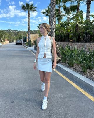 Woman wearing a white top, white miniskirt, and white sneakers.