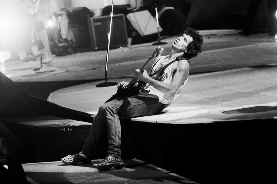 Keith Richards, sitting on stage, playing guitar with his eyes closed
