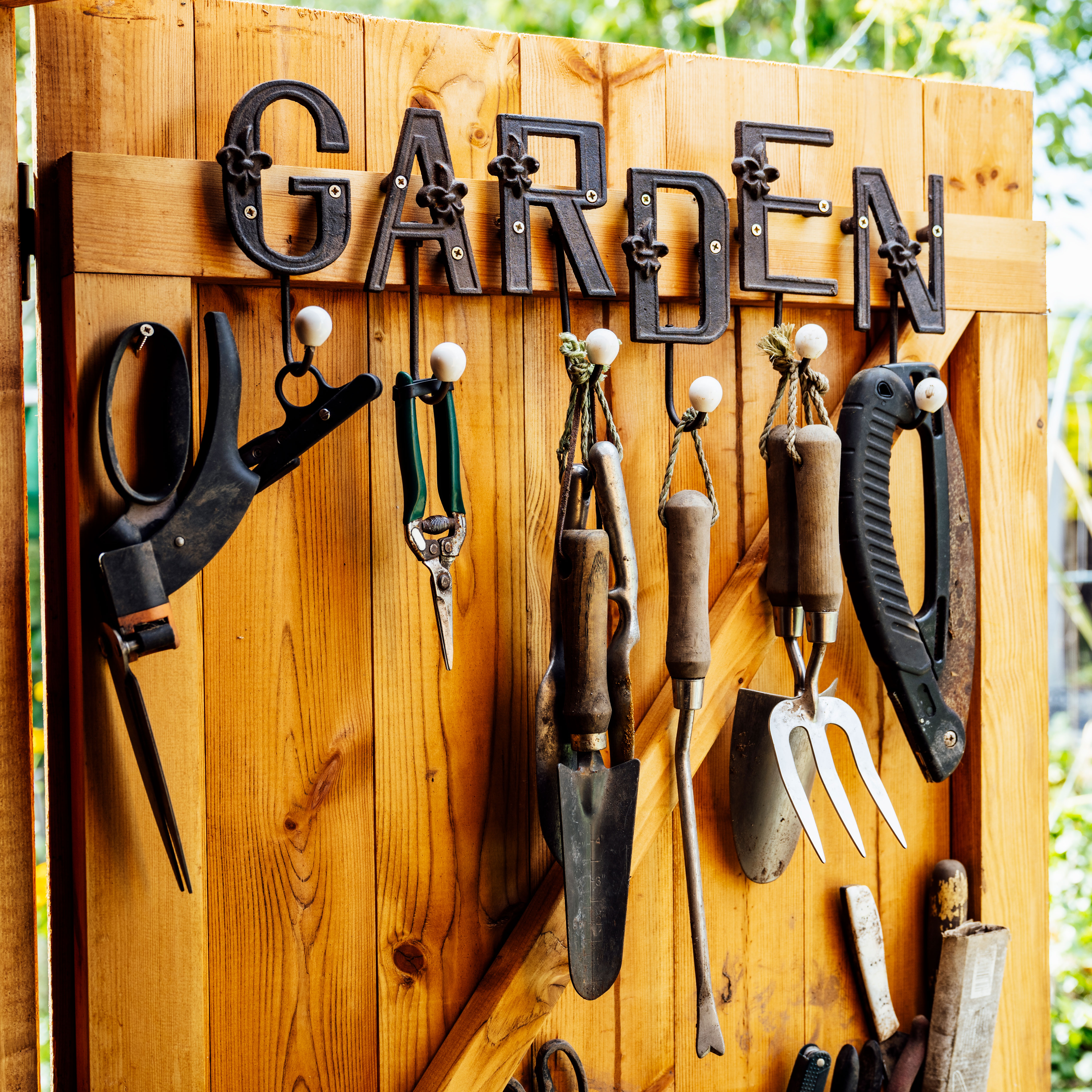 assorted garden tools hanging from rustic wooden shed door with garden sign