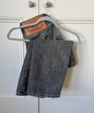 A pair of grey Diesel jeans on a grey velvet hanger hanging on a floral cupboard doorknob